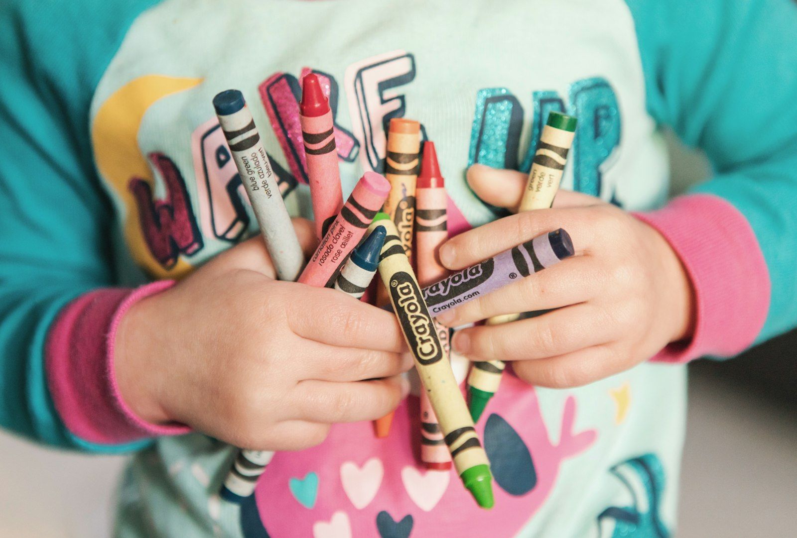 Kinderhände halten ein Bündel bunter Wachsmalstifte
