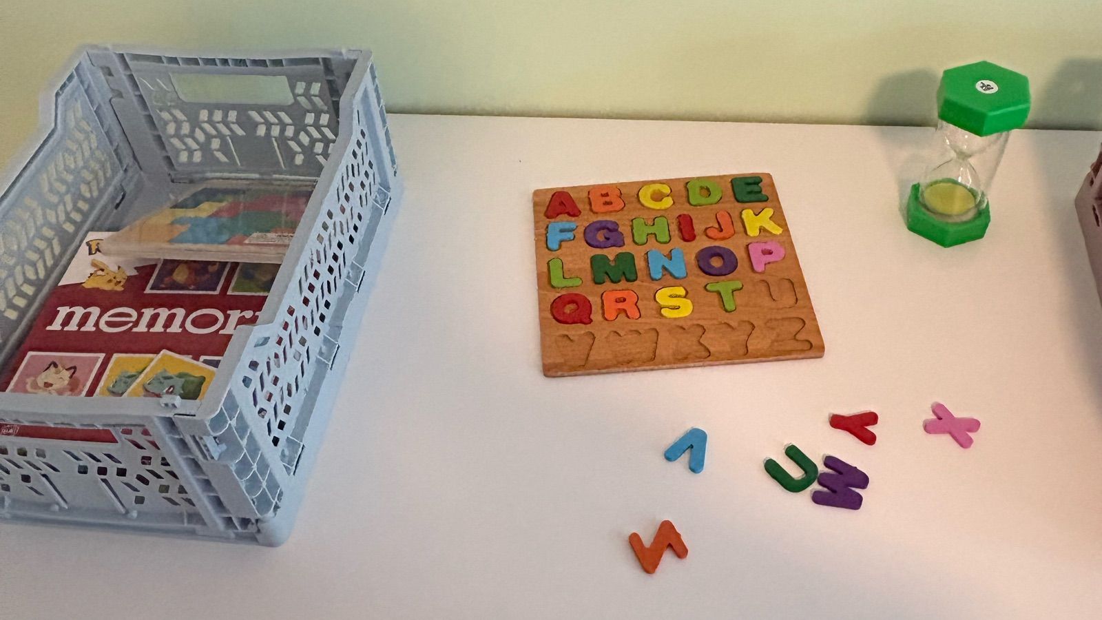 Lernmaterialien auf einem Tisch: Buchstabenpuzzle, Holzbuchstaben, Memory-Spiel und Sanduhr