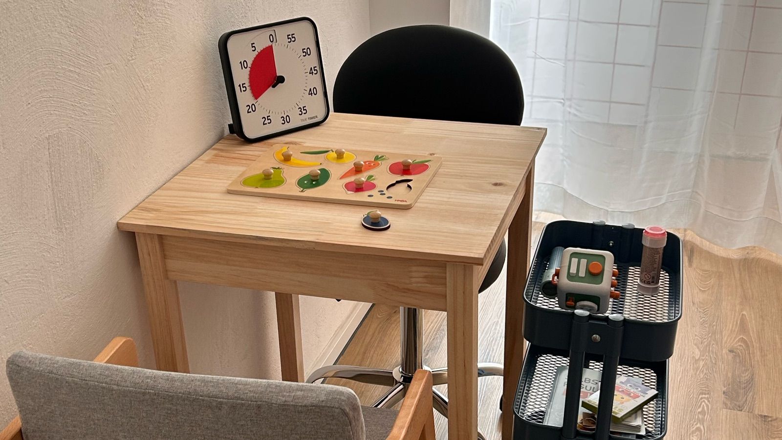 Kleiner Holztisch im 1:1-Therapieraum mit Time Timer, Holzpuzzle und Materialwagen